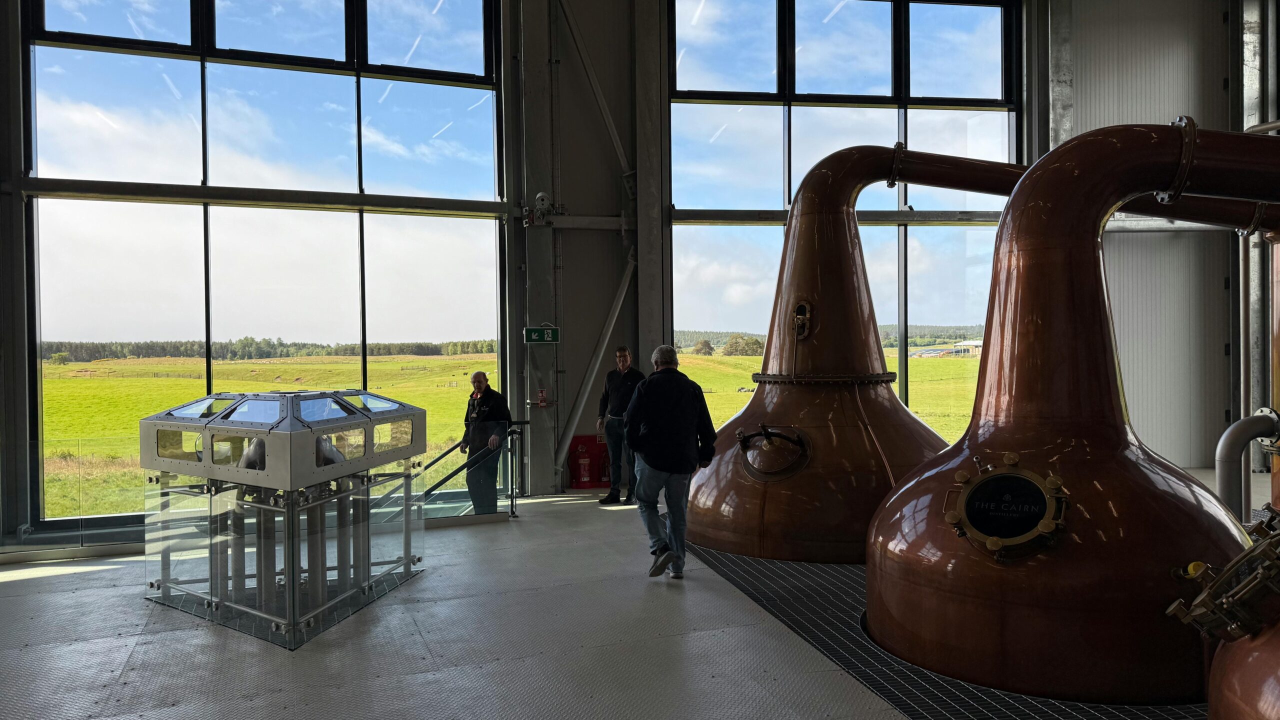 Copper whisky stills at a Glasgow distillery with scenic views through large windows