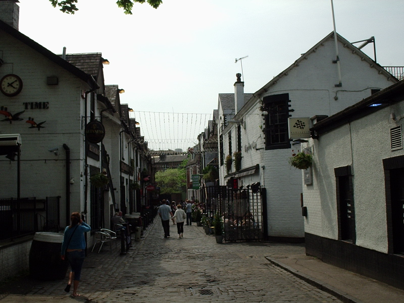 The cobbled Ashton Lane in Glasgow's West End, with whitewashed pubs on both sides, hanging baskets and strings of lights across the lane