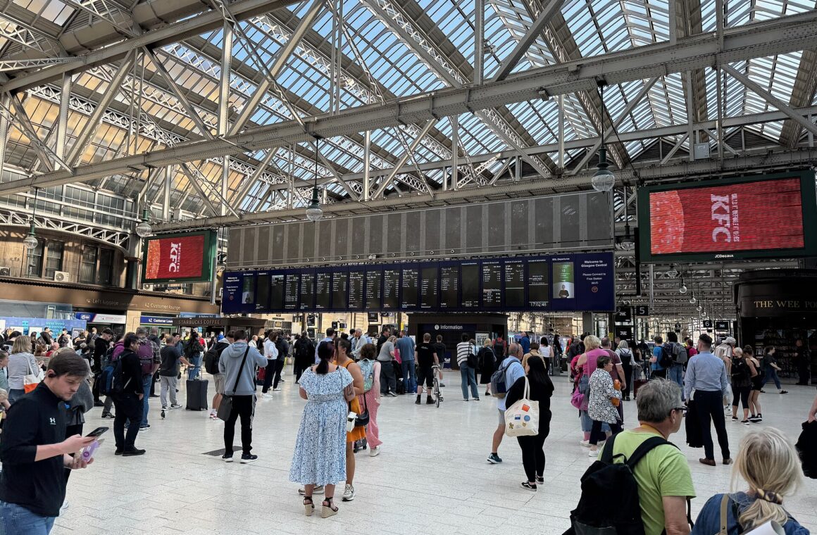 The busy main concourse at Glasgow Central Station under its glazed roof, with departure boards and crowds of passengers