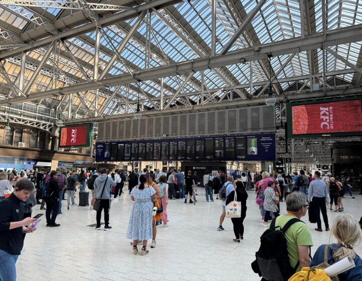 The busy main concourse at Glasgow Central Station under its glazed roof, with departure boards and crowds of passengers