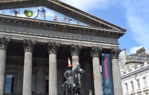 The Duke of Wellington statue, traffic cone on his head, in front of the columned portico of the Gallery of Modern Art on Royal Exchange Square