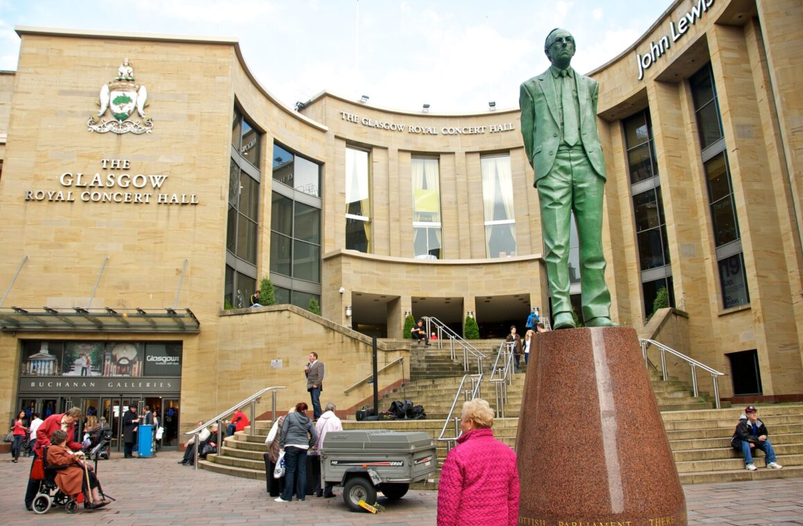 The curved sandstone front of the Glasgow Royal Concert Hall with its steps and the bronze statue of Donald Dewar in the foreground