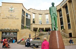 The curved sandstone front of the Glasgow Royal Concert Hall with its steps and the bronze statue of Donald Dewar in the foreground