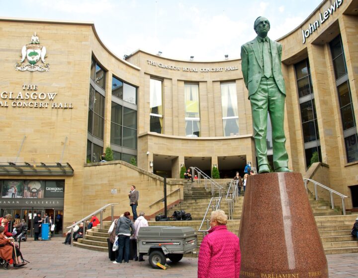 The curved sandstone front of the Glasgow Royal Concert Hall with its steps and the bronze statue of Donald Dewar in the foreground