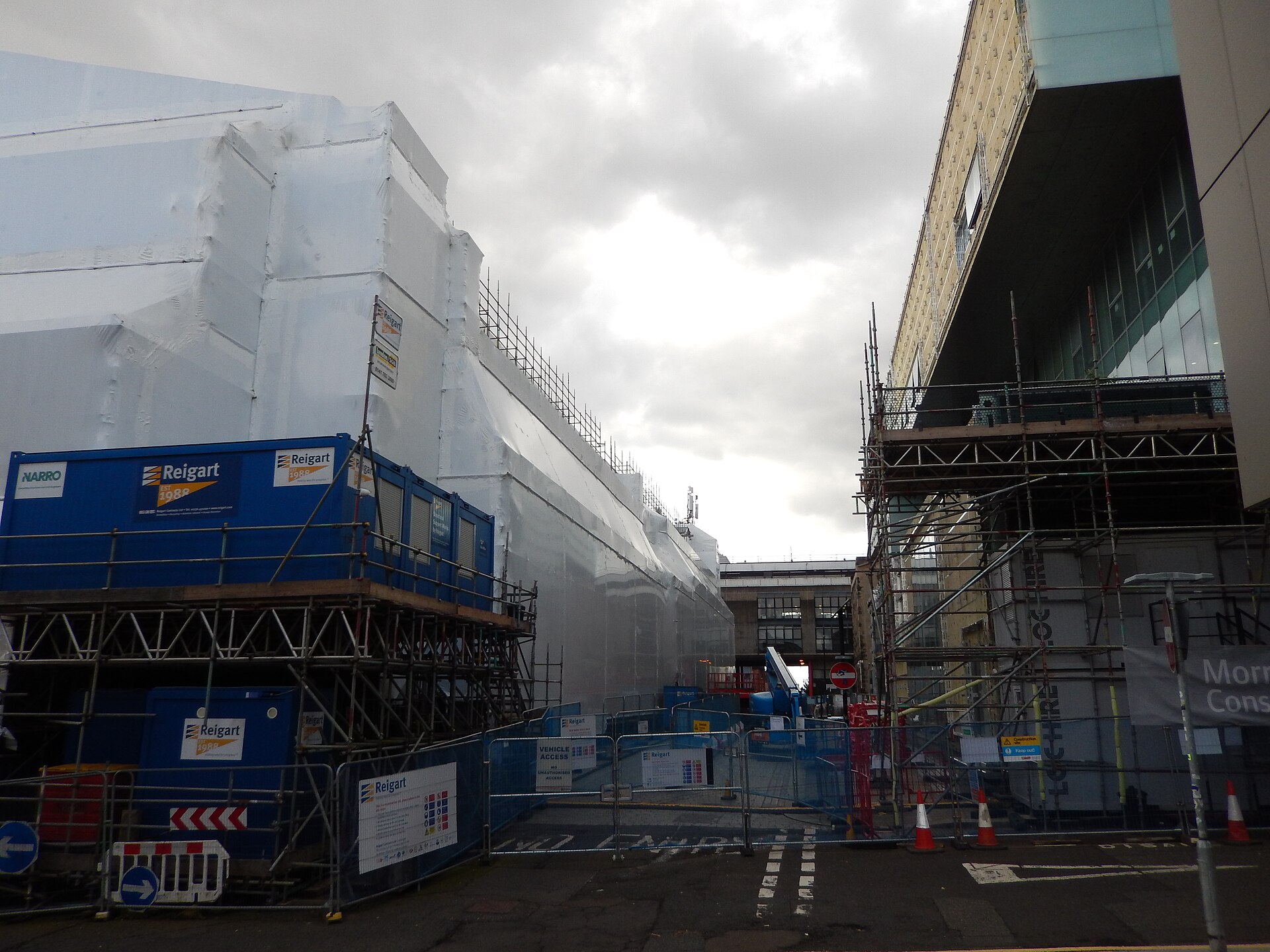 The fire-damaged Mackintosh Building of the Glasgow School of Art wrapped in white sheeting and scaffolding, opposite the modern Reid Building on Renfrew Street