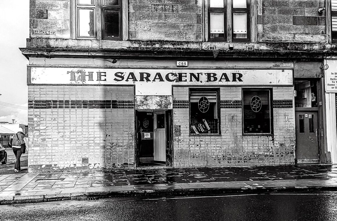 A tiled Victorian corner pub with THE SARACEN BAR painted above the windows on a wet Glasgow street