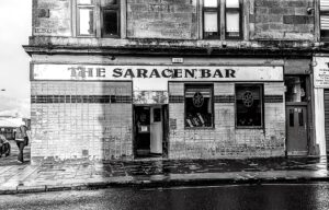 A tiled Victorian corner pub with THE SARACEN BAR painted above the windows on a wet Glasgow street