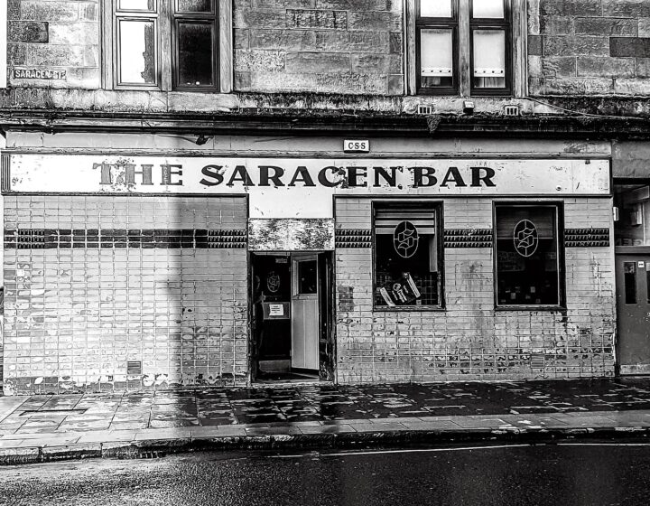 A tiled Victorian corner pub with THE SARACEN BAR painted above the windows on a wet Glasgow street
