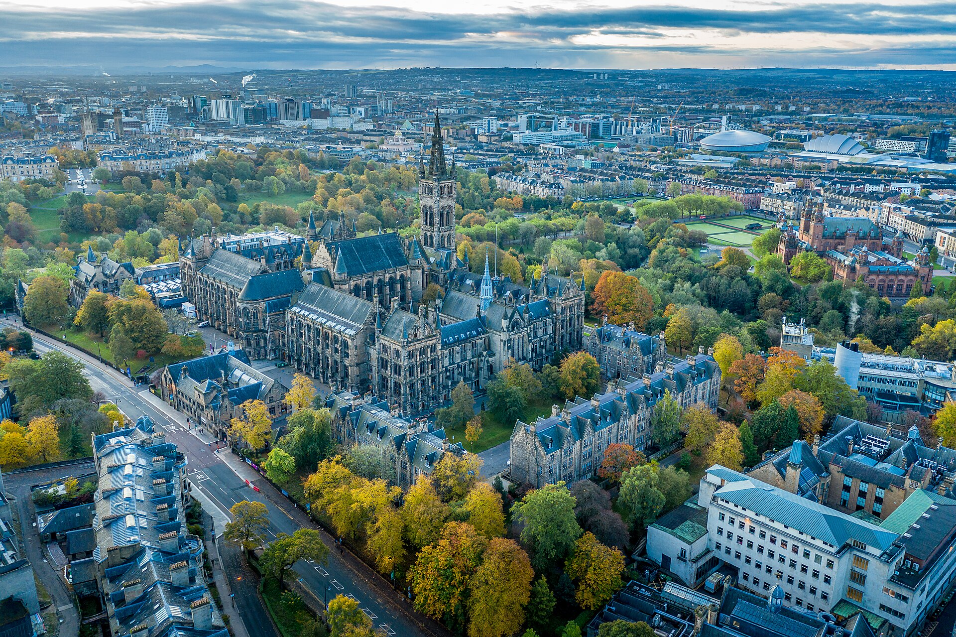 Aerial view of the University of Glasgow's Gothic main building among autumn trees, with Kelvingrove Art Gallery to the right and the city centre, SEC Armadillo and OVO Hydro beyond