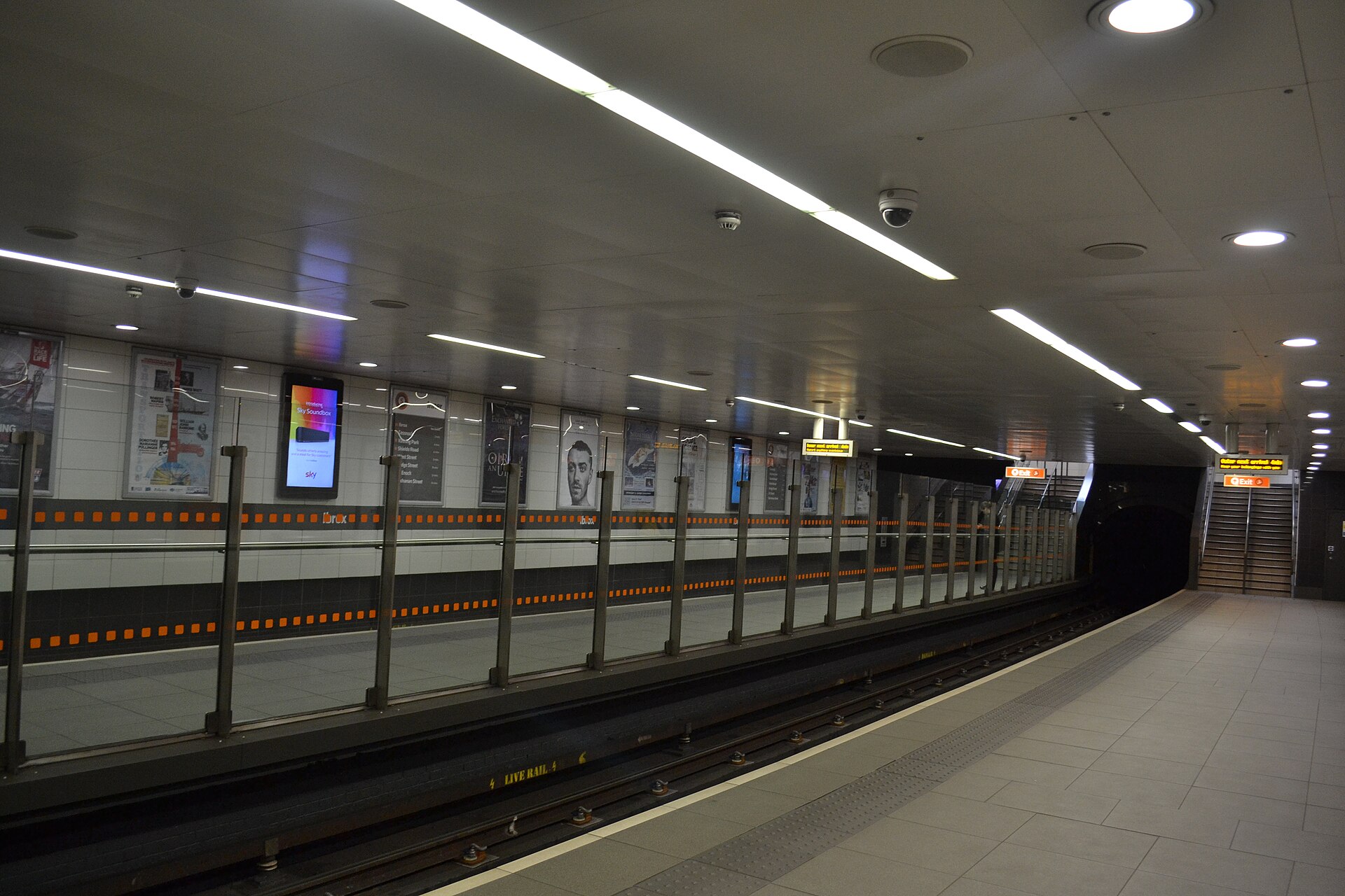 The tiled platform at Ibrox Subway station with orange station banding and the exit stairs at the far end