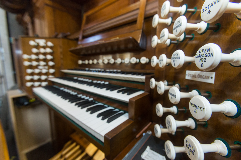 The wooden console of the Kelvingrove pipe organ, with three keyboards and rows of white stop knobs labelled Open Diapason and Trumpet