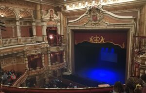 The ornate gilded auditorium of the King's Theatre Glasgow, with red and cream boxes beside the stage, a crown above the proscenium and blue light on the curtain