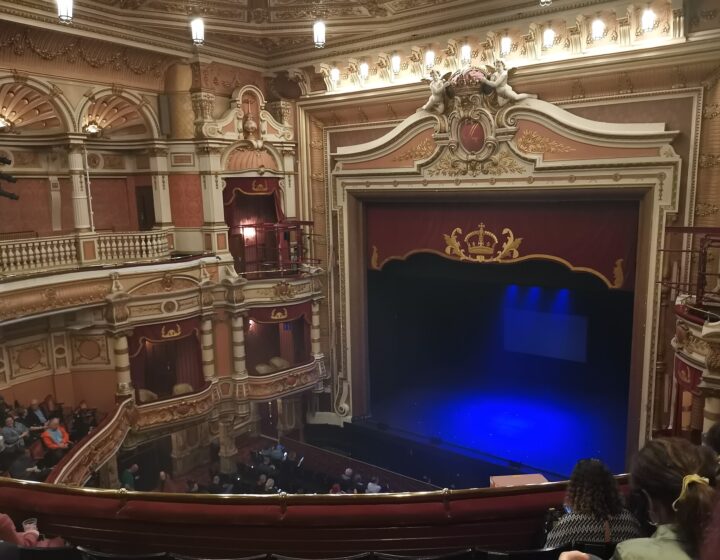 The ornate gilded auditorium of the King's Theatre Glasgow, with red and cream boxes beside the stage, a crown above the proscenium and blue light on the curtain
