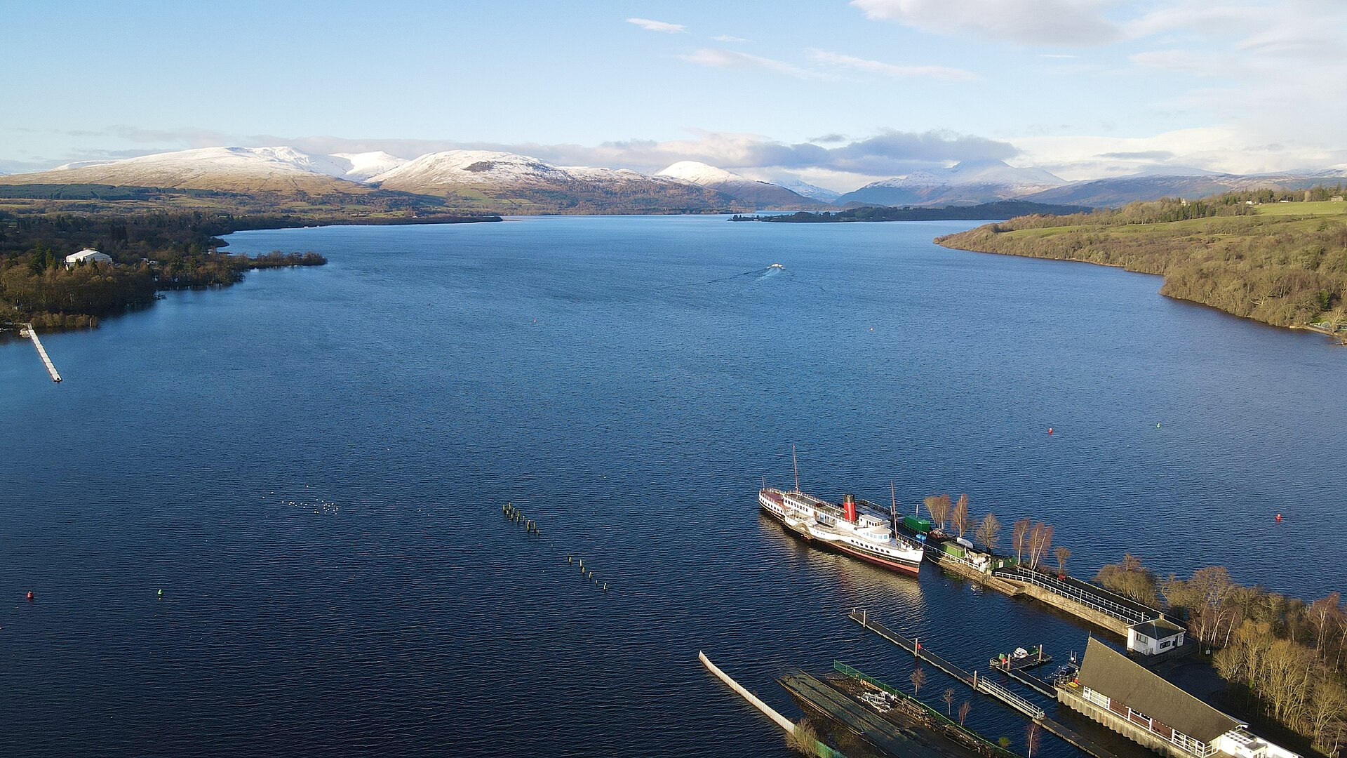 Aerial view of Loch Lomond from Balloch, with the paddle steamer Maid of the Loch at the pier in the foreground and snow-capped hills beyond the water