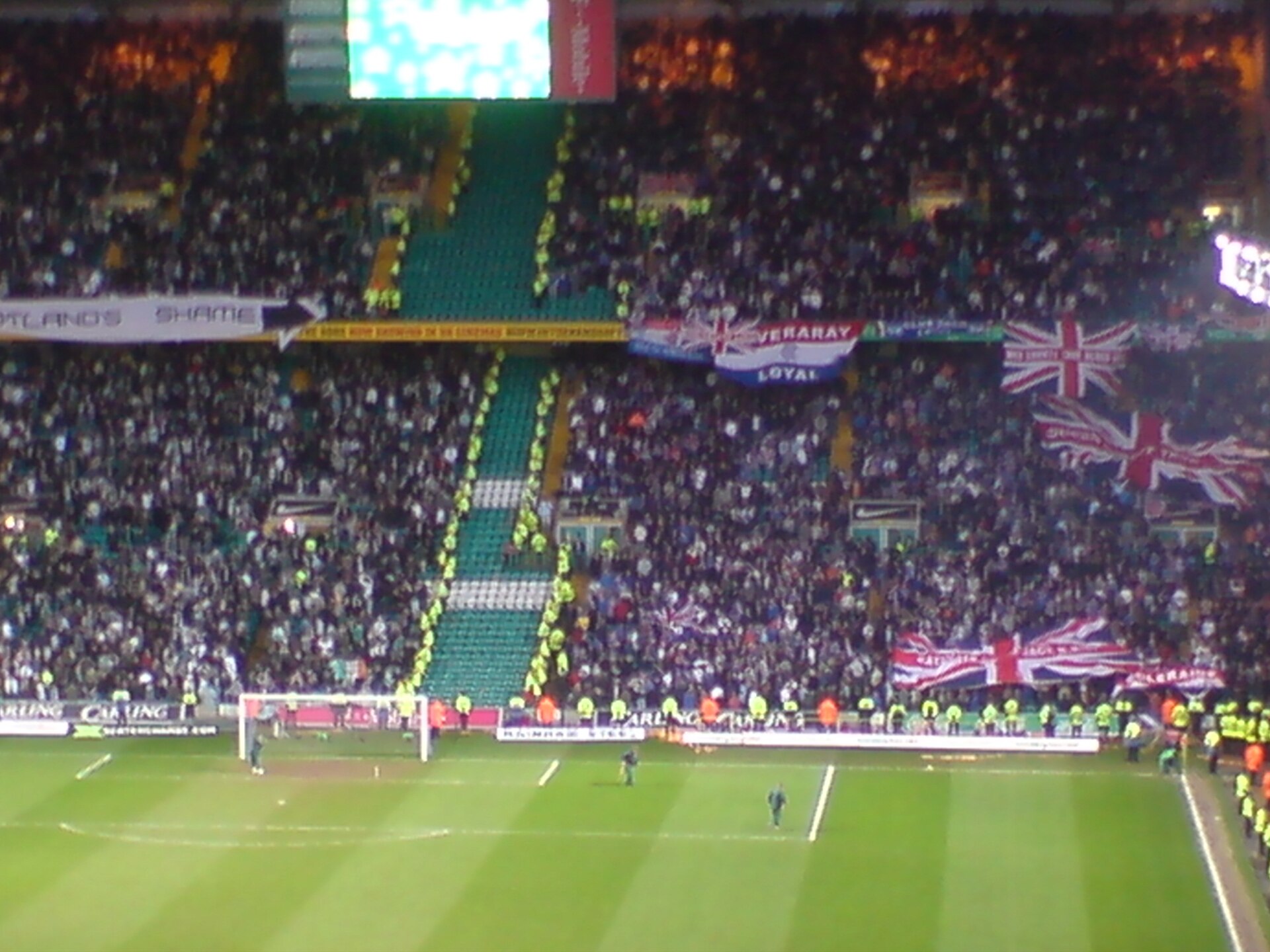 A block of empty green seats and a double line of hi-vis stewards separating home and away supporters inside a packed Celtic Park during an Old Firm derby