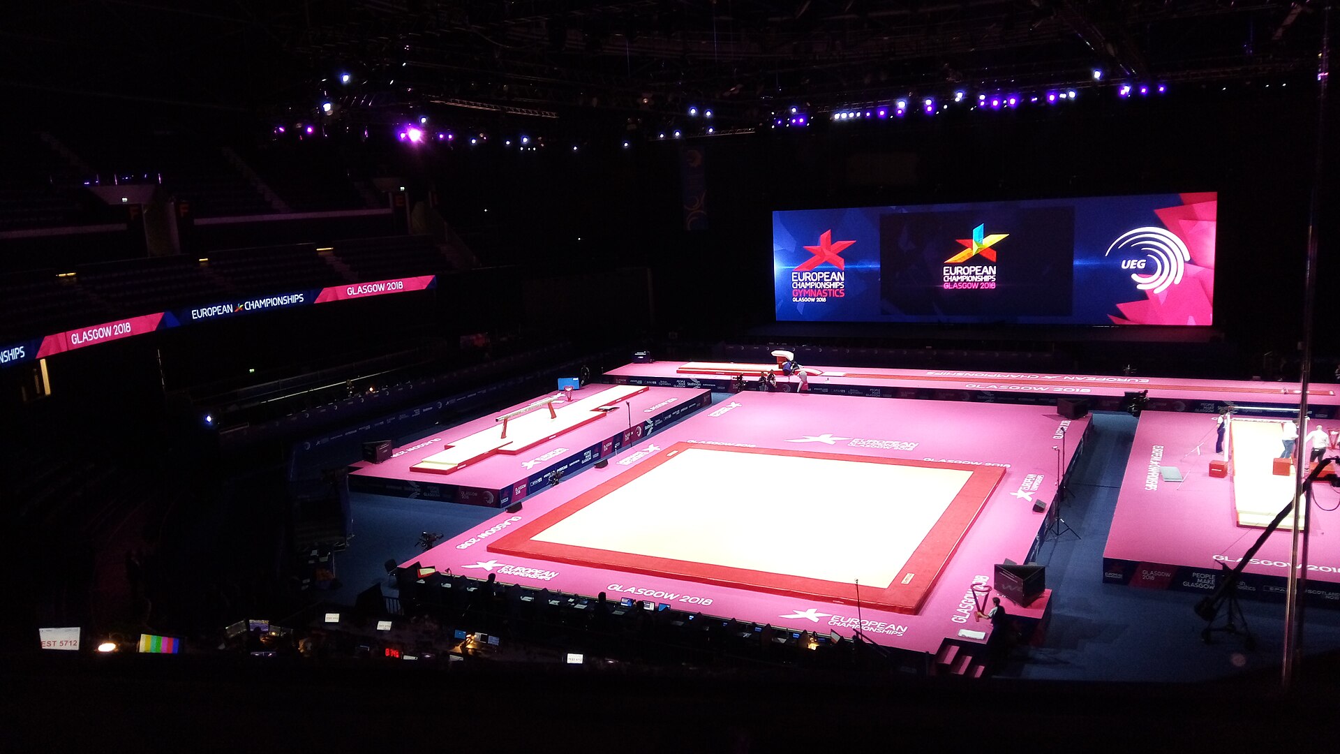 Inside the arena set up for gymnastics, with the floor lit in pink and the steep banks of seats rising into darkness on either side