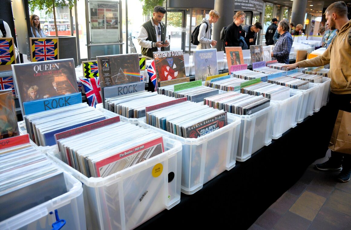Rows of plastic crates full of LPs at an outdoor record fair, with shoppers browsing along the tables