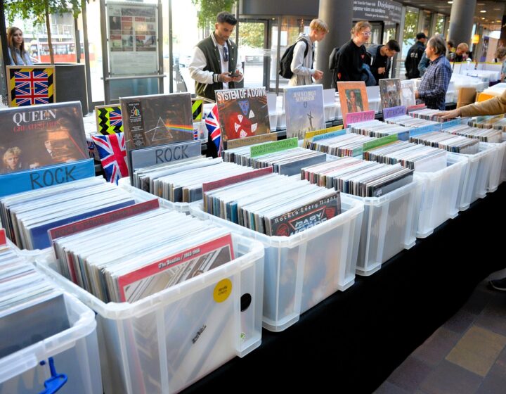 Rows of plastic crates full of LPs at an outdoor record fair, with shoppers browsing along the tables