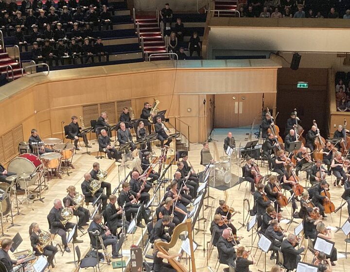 The Royal Scottish National Orchestra on a wide wooden stage seen from above, with the audience seated on tiers around the hall