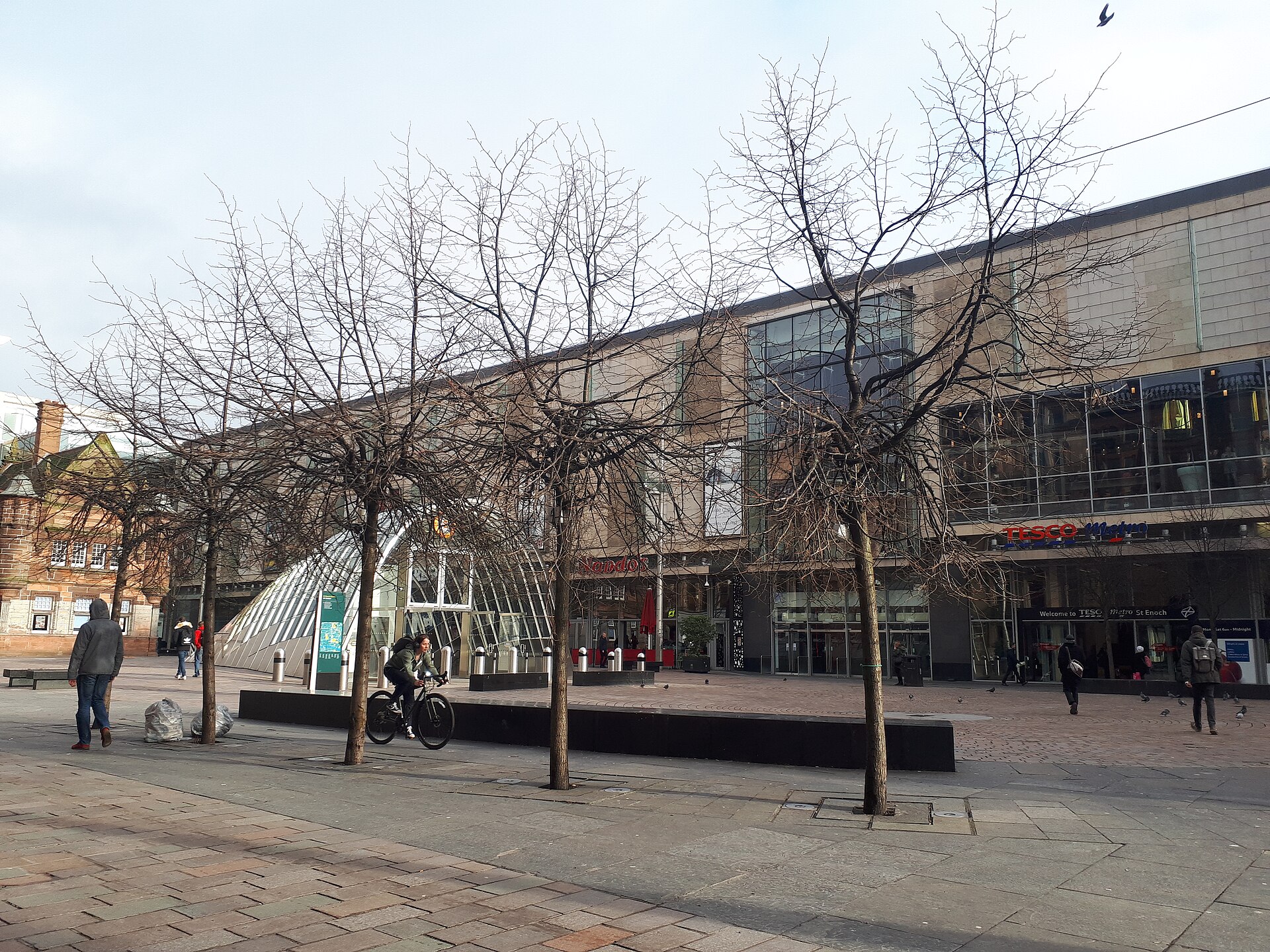 St Enoch Square on a bright winter day, with bare trees, the curved glass St Enoch Subway entrance and the St Enoch Centre behind