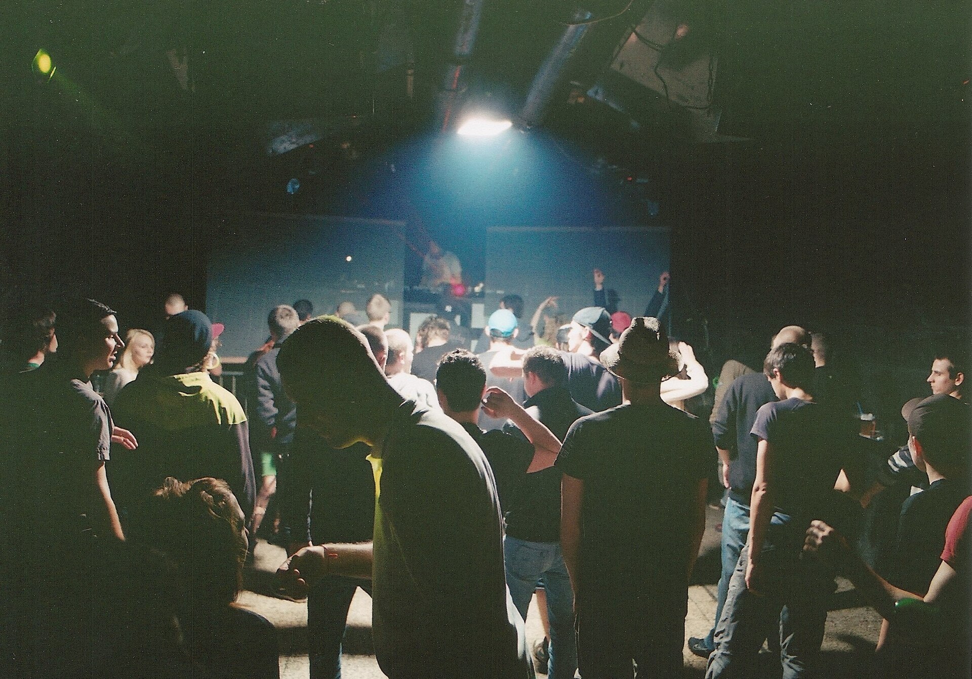 Silhouetted clubbers on a dark dance floor facing a DJ booth lit by a single blue light