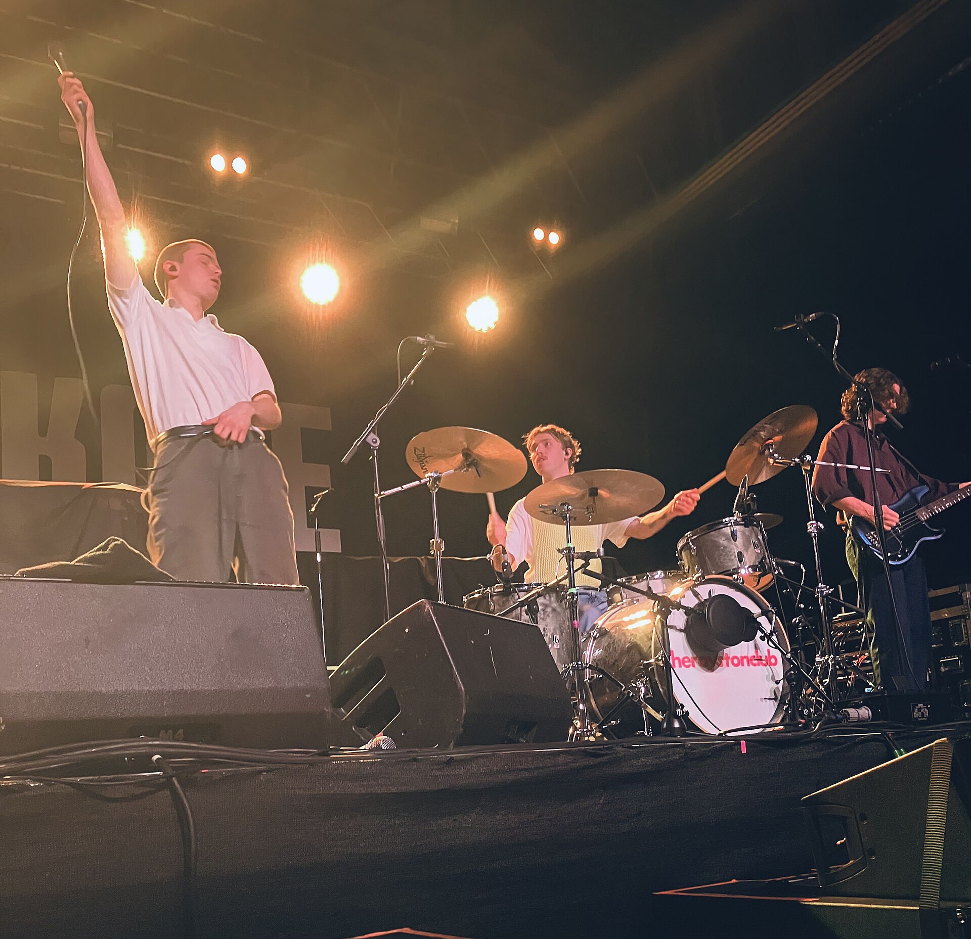 A four-piece guitar band on stage at SWG3, the singer with one arm raised towards the lights and the drummer mid-hit