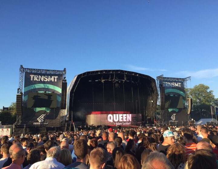 The TRNSMT main stage on Glasgow Green under a clear blue sky, with a large crowd in front of the stage and the headline act's name on the screen