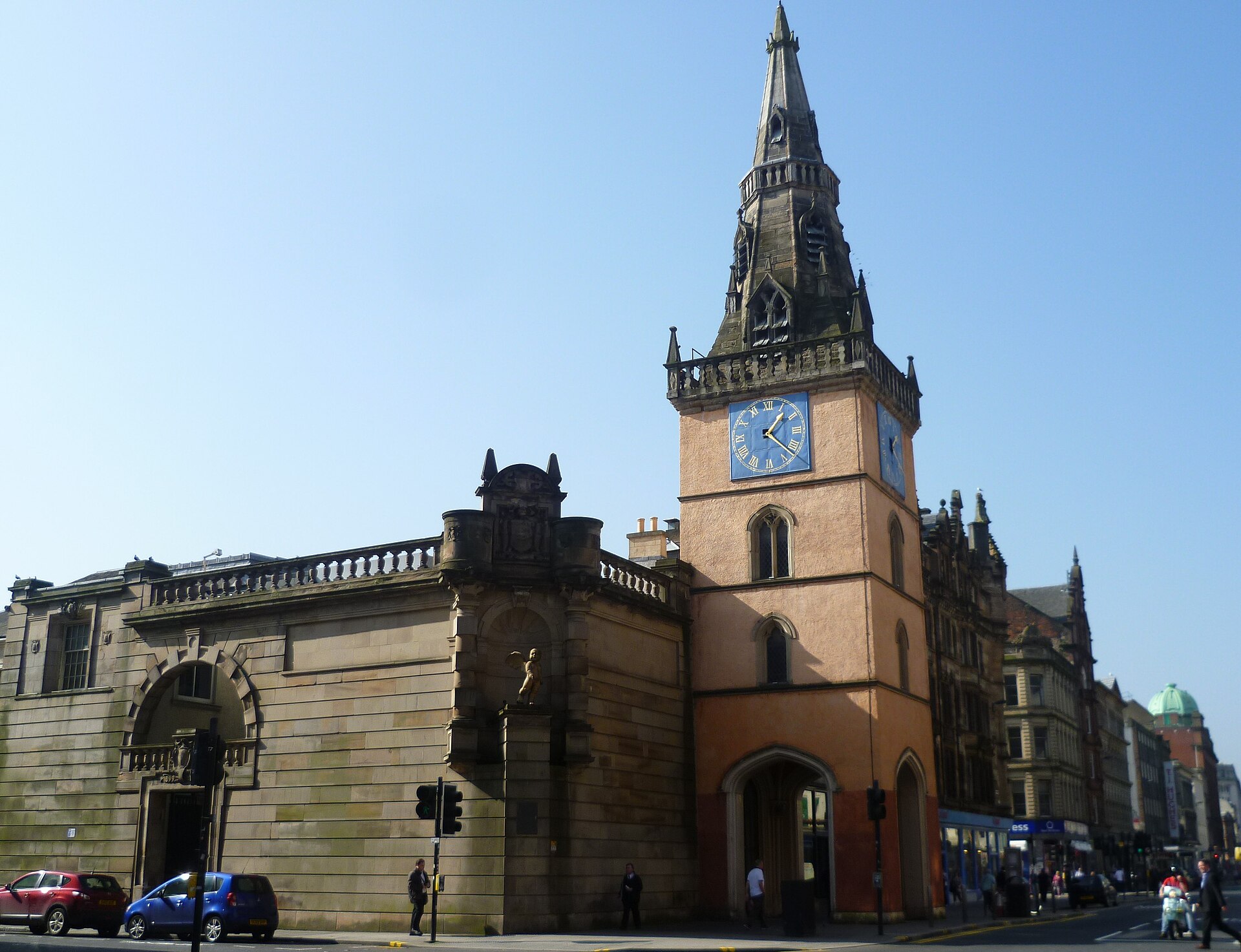 The Tron Theatre on the Trongate, with its stone clock tower and spire rising above the corner entrance under a blue sky