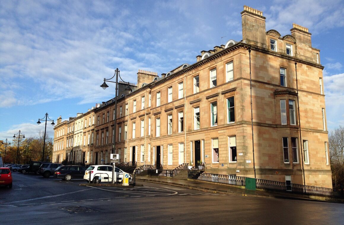 Sunlit sandstone terrace curving along Park Circus Place in Glasgow's West End, with old-style lamp posts and autumn trees