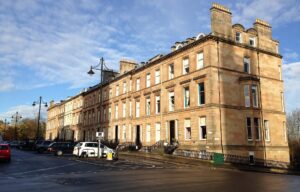 Sunlit sandstone terrace curving along Park Circus Place in Glasgow's West End, with old-style lamp posts and autumn trees