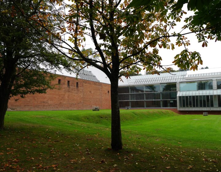 The red sandstone and glass Burrell Collection building beyond a sloping lawn and a horse chestnut tree in early autumn, in Pollok Country Park